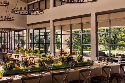 Elegant indoor wedding reception at Four Seasons Orlando at Walt Disney World Resort featuring long guest tables decorated with lush sunflower centerpieces and green grass arrangements, set in a bright, modern ballroom with floor-to-ceiling windows overlooking tropical greenery