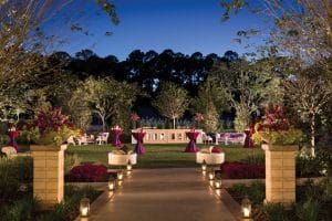 Elegant outdoor wedding reception setup at Four Seasons Orlando at Walt Disney World Resort, featuring a candlelit pathway lined with lush planters, vibrant fuchsia floral arrangements, and softly lit dining tables under twilight skies in Orlando Florida