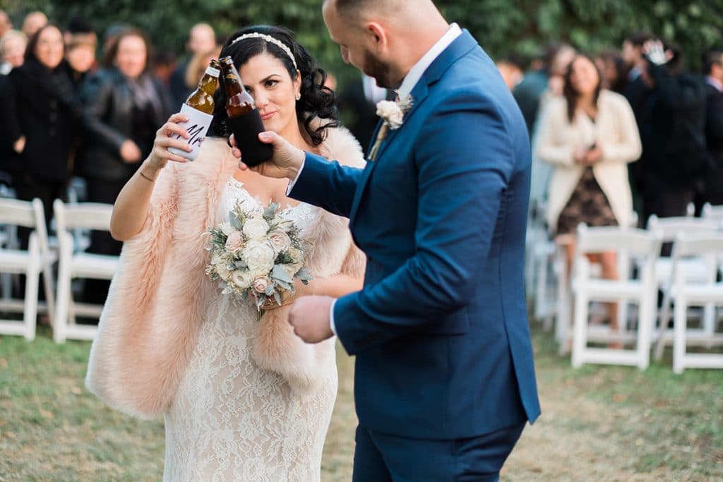 bride and groom toasting each other with beer bottles