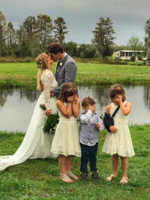 Mystical Winds bride and groom kissing outside with kids covering their eyes