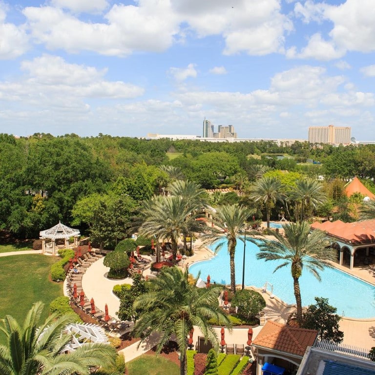 view from hotel balcony overlooking palm trees and pool with orlando skyline in background