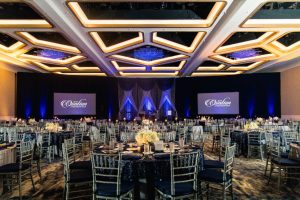 hotel ballroom set up for conference with round tables, dark chairs, and ceiling light grid