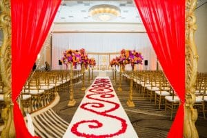 wedding ceremony set up in hotel ballroom with gold chairs and archway and elaborate red floral decor