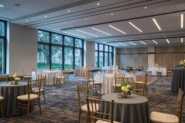 hotel ballroom set up for wedding reception with small round tables, gold chairs, and large windows