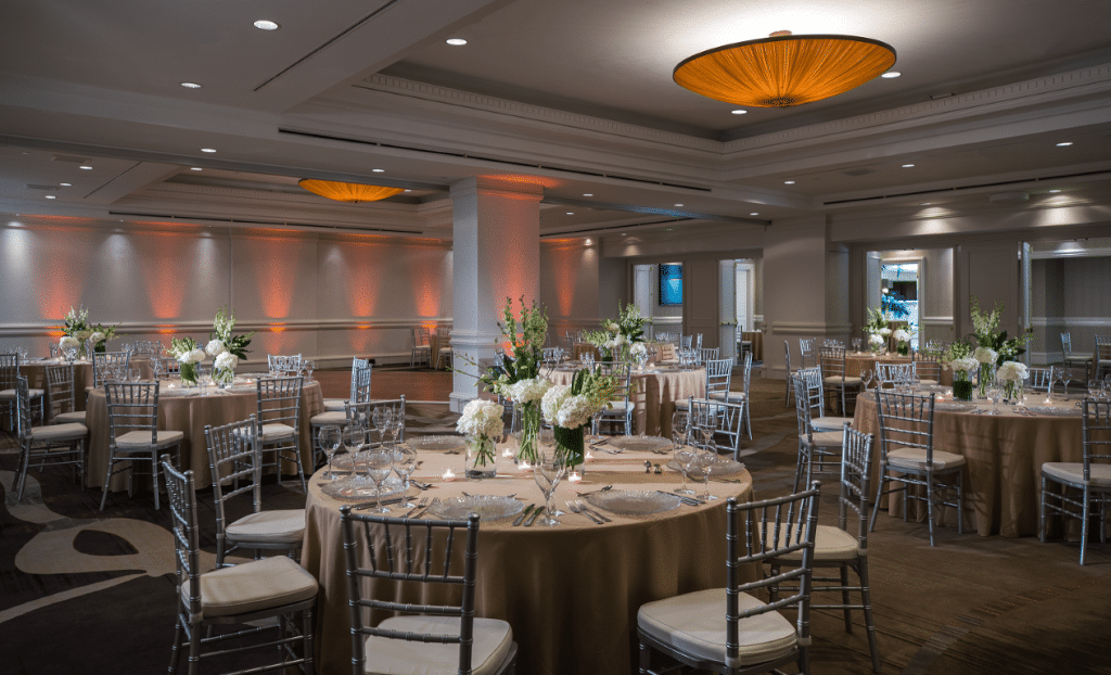 hotel ballroom set up for wedding reception with gold linens, white flowers, and orange lighting