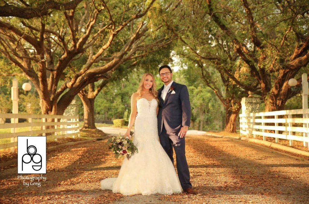The-Highland-Manor-Bride and Groom standing on dirt road under overhanging trees next to a white picket fence