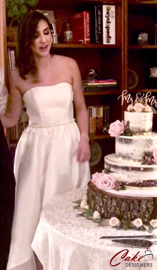 bride standing next to rustic 4 tier cake