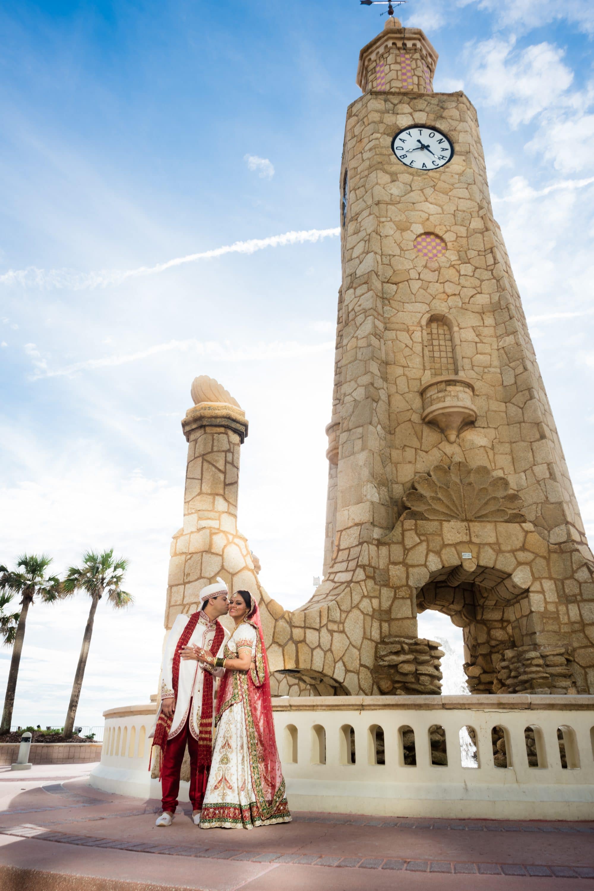 Indian bride and groom posing beside tall stone tower