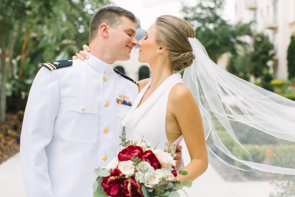 groom in white military uniform with bride holding red and white bouquet