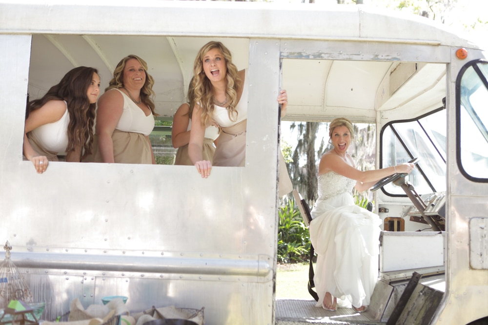 Bride pretending to drive old food truck while bridesmaids peek out