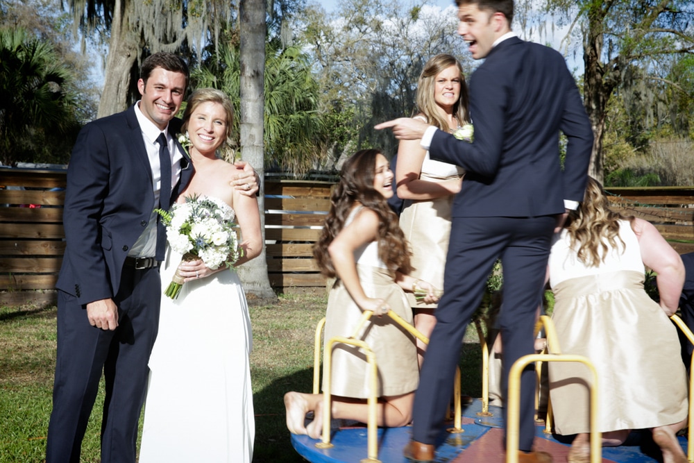 bride and groom posing while bridal party plays on merry-go-round