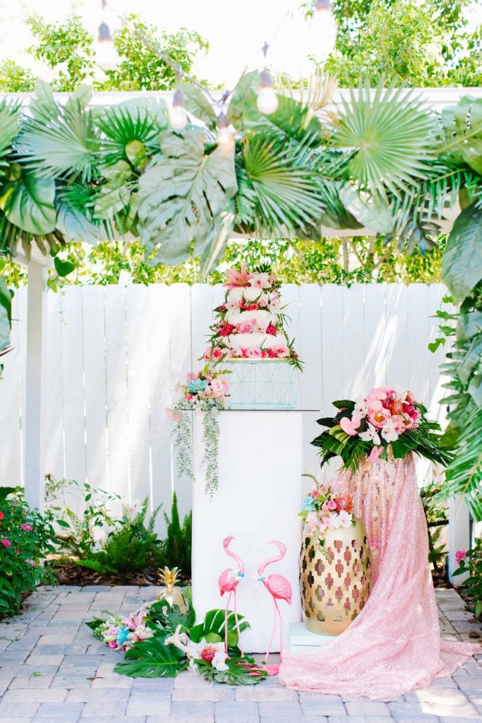 tropical wedding cake display with white picket fence and pink flamingos from Atmospheres Floral