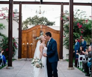 Venue-650-Bride and Groom kissing in courtyard in front of large wooden gate