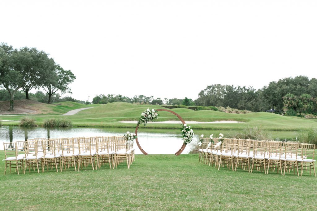outdoor ceremony setup with circular arch set against a lake by Bumby Photography