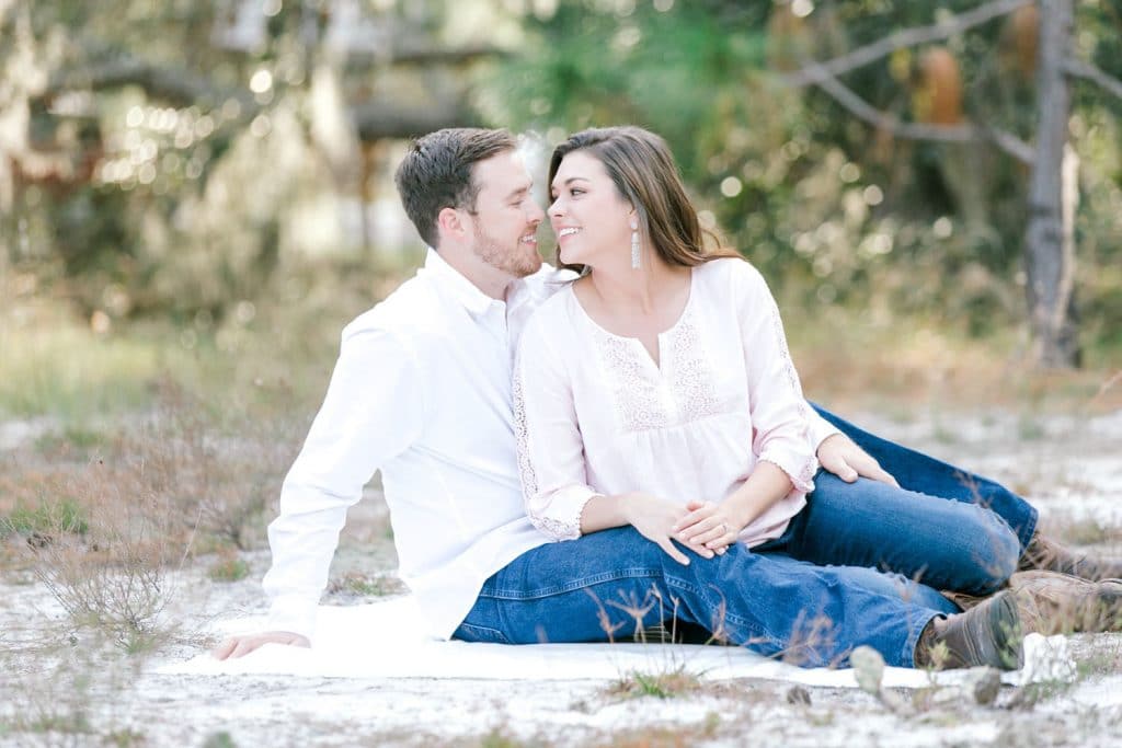 couple sitting on blanket outside in white shirts and jeans by Bumby Photography