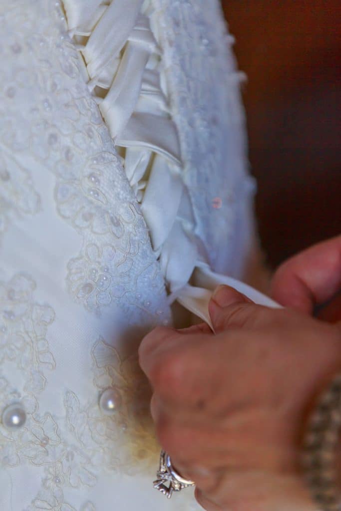 With This Ring - hands lacing up back of wedding dress