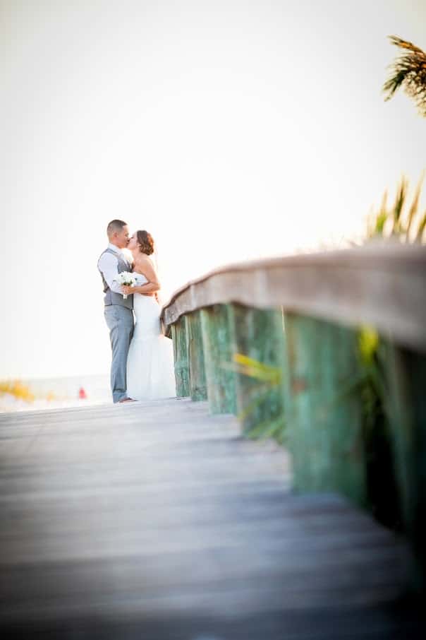 With This Ring - bride and groom kissing at the end of beach boardwalk