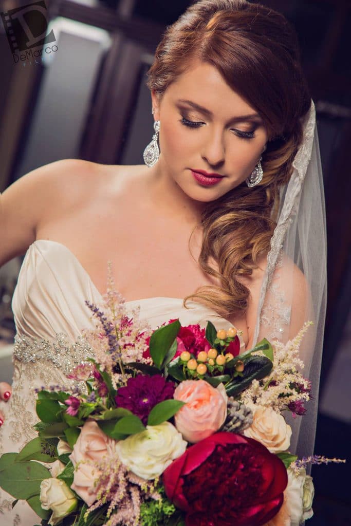 bride looking down at stunning bouquet of mixed flowers and hair and make-up by kristy's artistry design team
