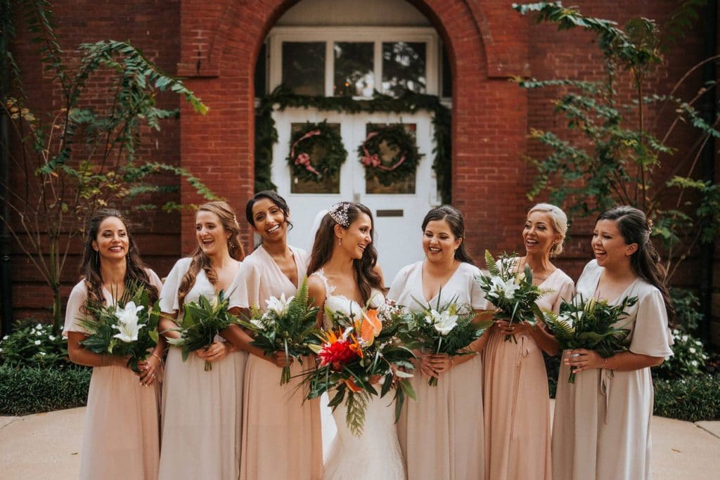 bride with bridesmaids in varying shades of peach and hair and make-up by kristy's artistry design team