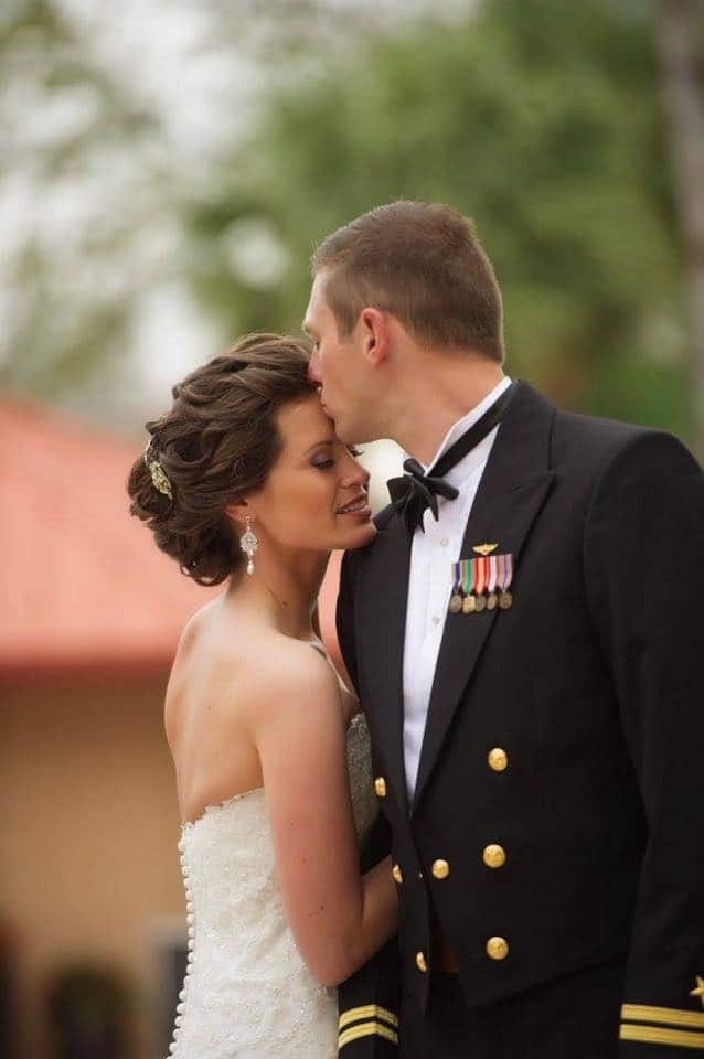 groom in dress uniform kissing bride on forehead with make-up and hair by kristy's artistry design team