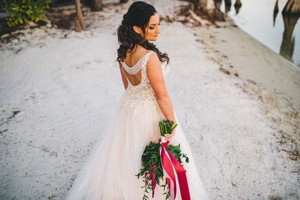 bride standing on white sand aisle with hair and make-up by kristy's artistry design team
