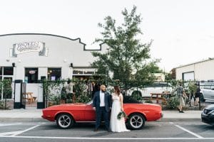 1010-West-Bride and Groom standing in front of older model car outdoors