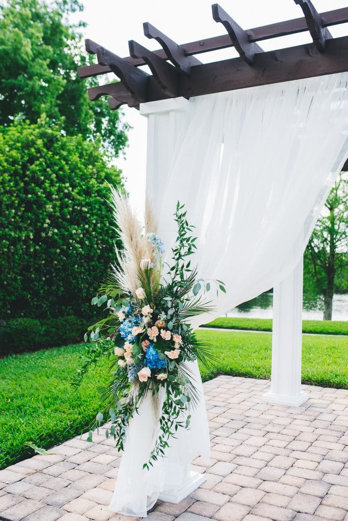 The Flower Studio - pergola with blue flower spray with pampas grass and white fabric
