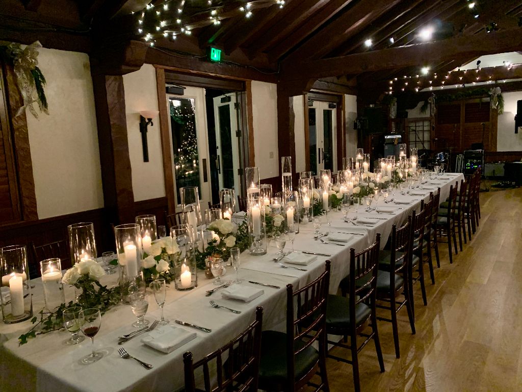 Fairbanks Florist centerpieces on long table with white table settings and many candles in room with wood beams
