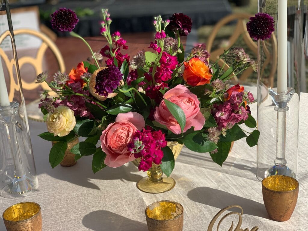 small pink and yellow floral arrangement in gold vase surrounded by gold votives by Fairbanks Florist