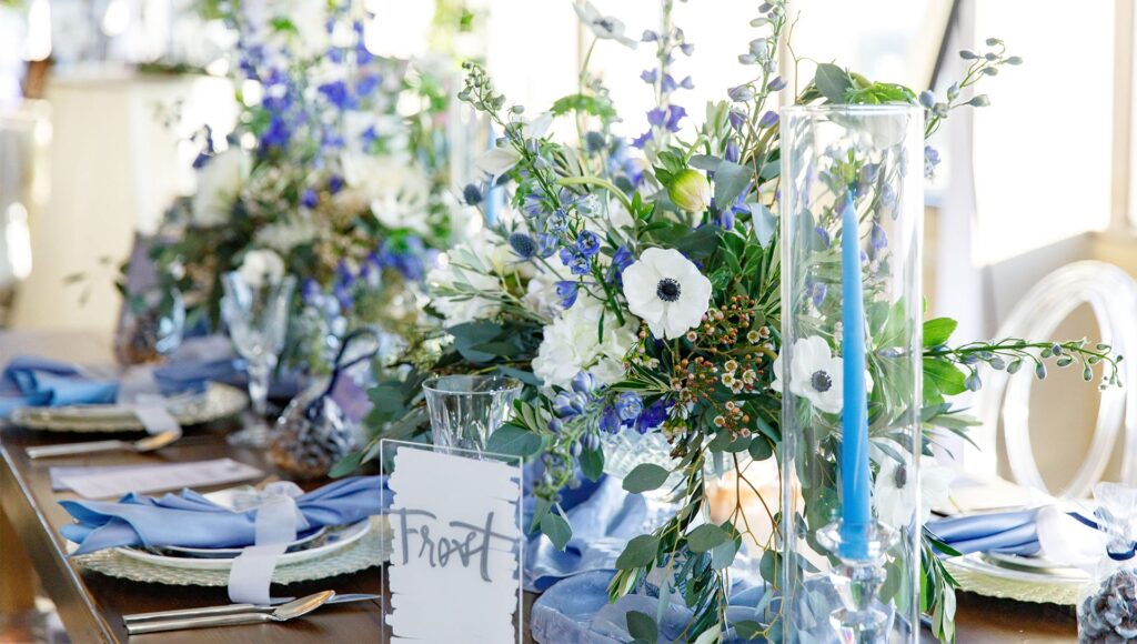 large blue and white floral arrangements on table with blue table settings for wedding reception by Fairbanks Florist