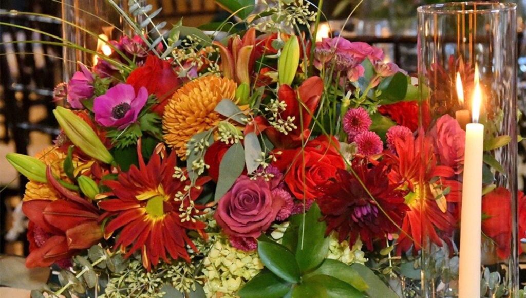 red pink and yellow floral arrangement with tall candle in front