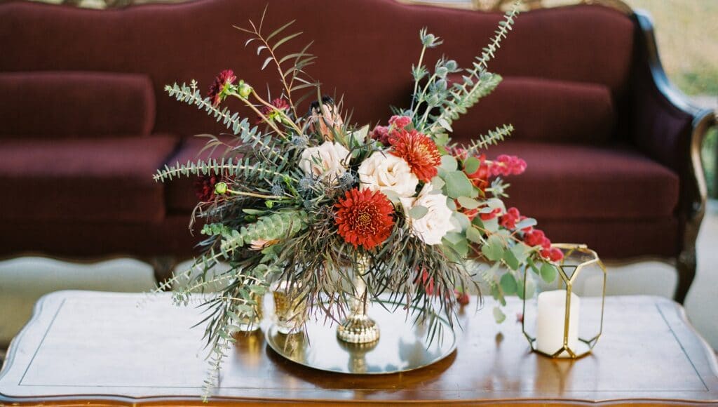 white and red rose bouquet with large greenery on table in front of dark red couch
