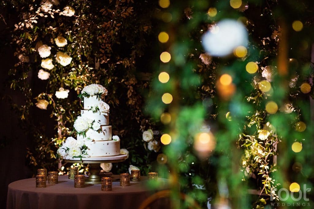 Fairbanks-Florist- Greenery wall with white wedding cake in front with lights