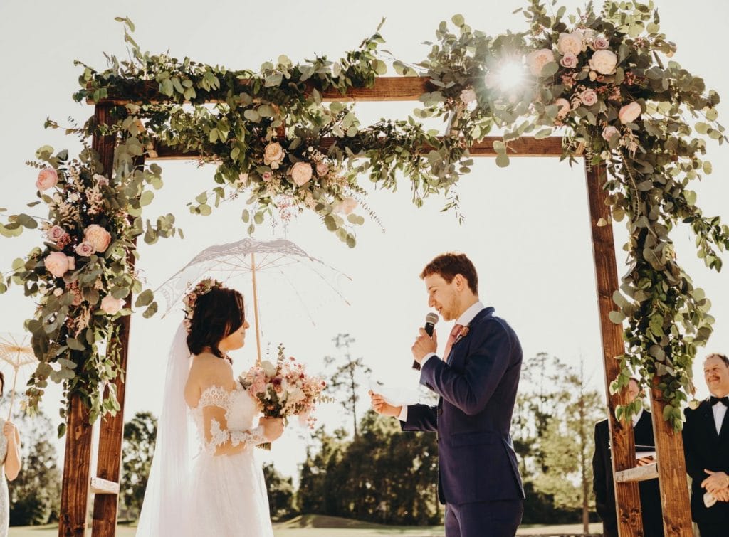 Square wedding arch with greenery and light pink flowers with bride and groom vows by Fairbanks Florist