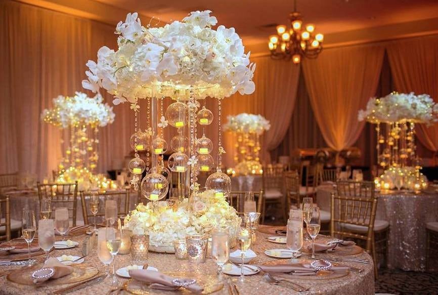 Dinner table settings with tall white floral lit centerpieces and crystal bubble chandelier hanging down by Fairbanks Florist