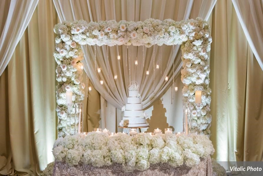 Variety of white flowers in square arch spotlighting wedding cake by Fairbanks Florist