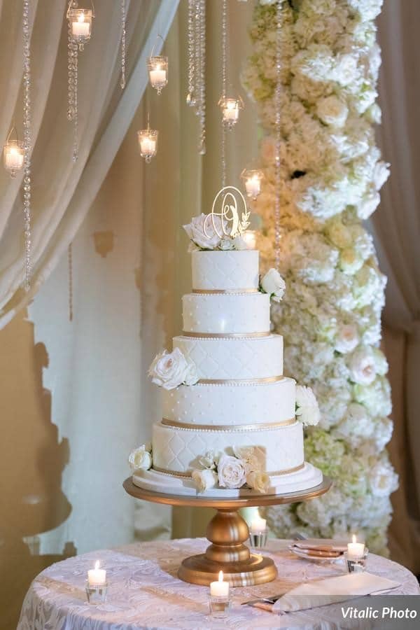 Fairbanks-Florist- Wedding cake on gold cake stand with part of white floral arch in background