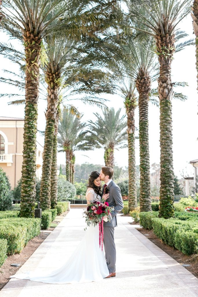bride and groom kissing on a path between palm trees by Bumby Photography