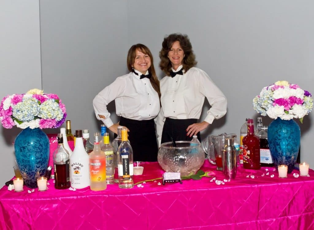 Orlando-Party-Servers-Two bartenders posing for picture behind bright pink table with flowers and punch bowl