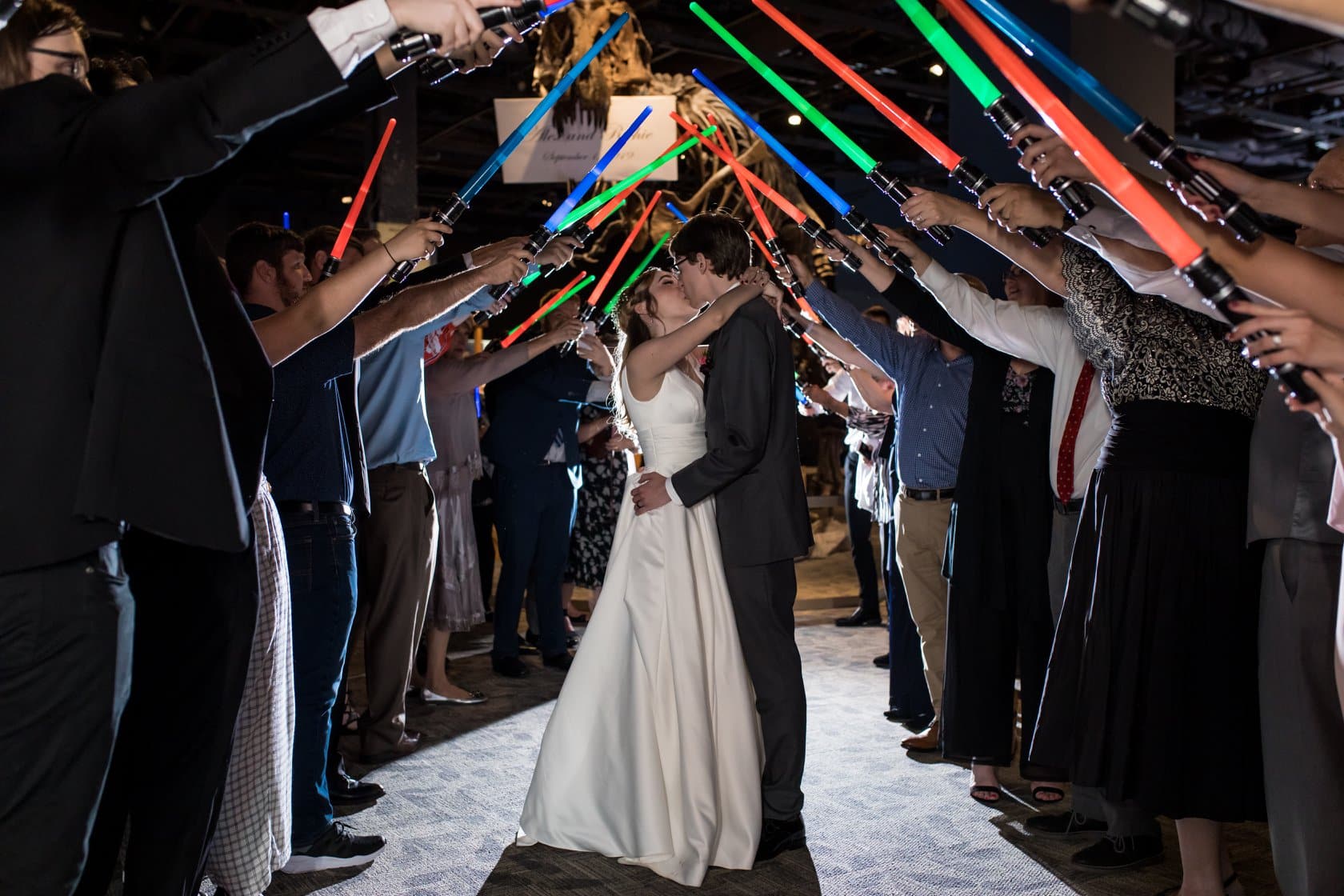 Bride & groom kissing under guests holding up lightsabers