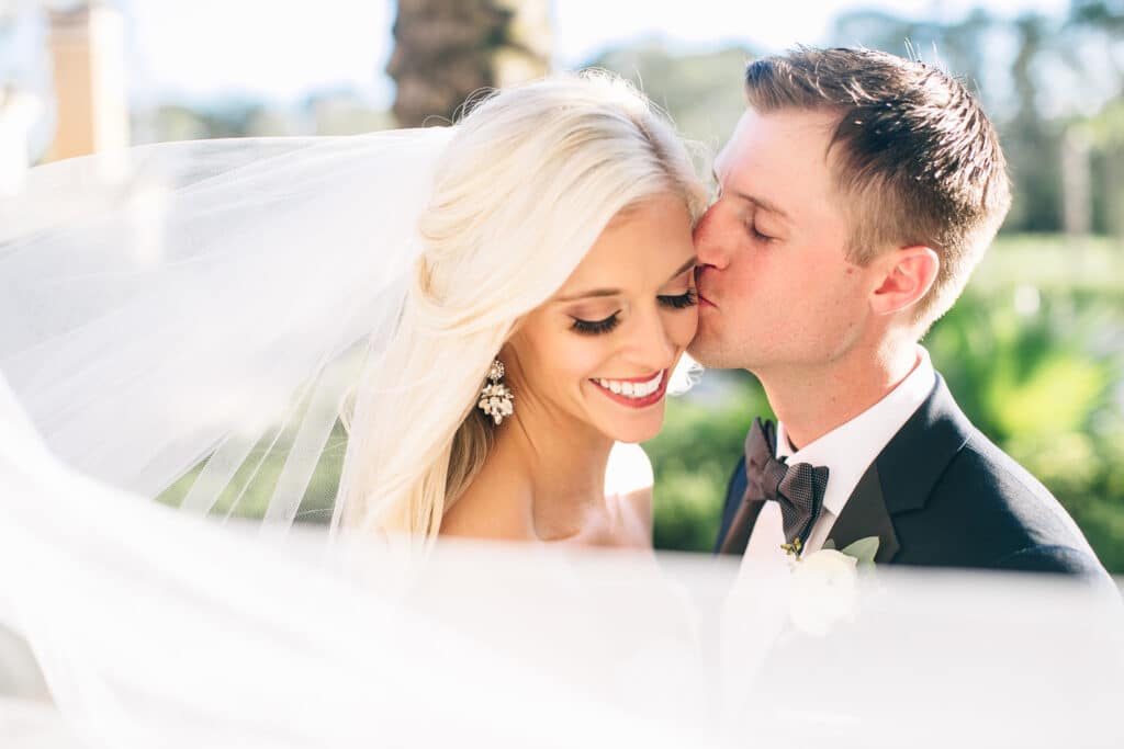 groom kissing bride on cheek with veil floating in foreground