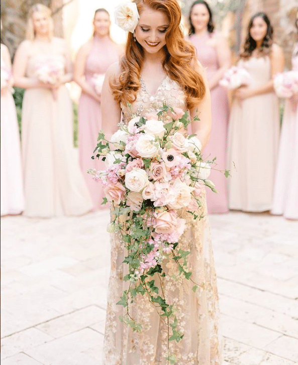 bride smiling and looking down at her bouquet while her bridesmaids look on