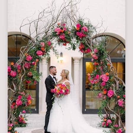 bride and groom hugging under a flower and vine covered arch