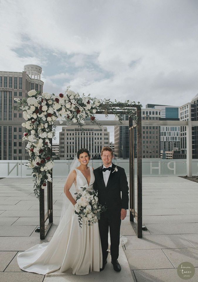 bride and groom standing next to arch on building roof in downtown