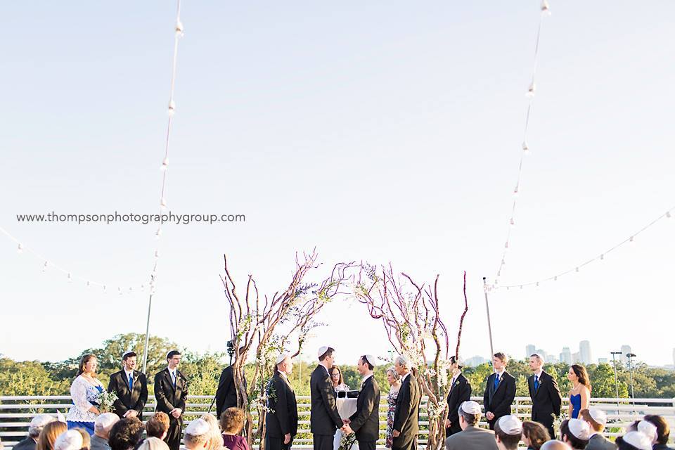 Grooms getting married during outdoor wedding ceremony with large branch arches
