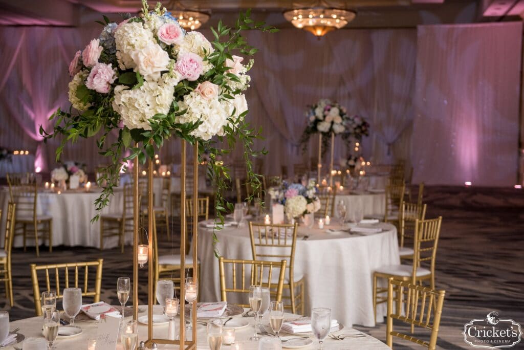 ballroom decorated for wedding reception with white and pink flowers and matching curtains and uplights
