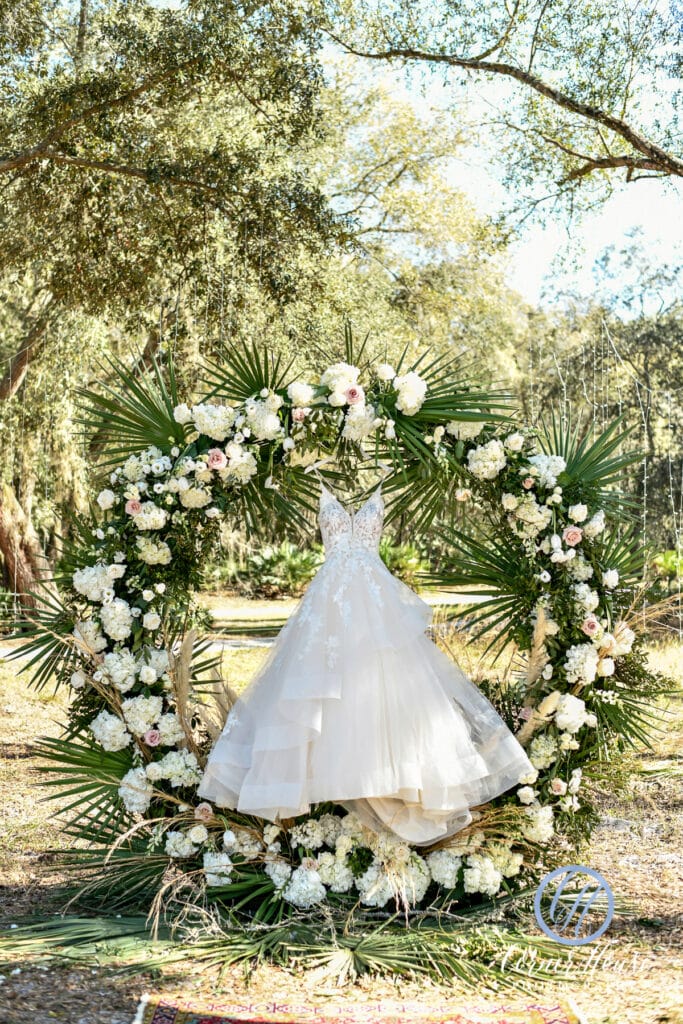 brides dress handing from circle arch covered in green and white flowers