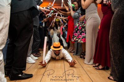 man sliding on floor toward camera with wedding guests on either side of him holding glow sticks