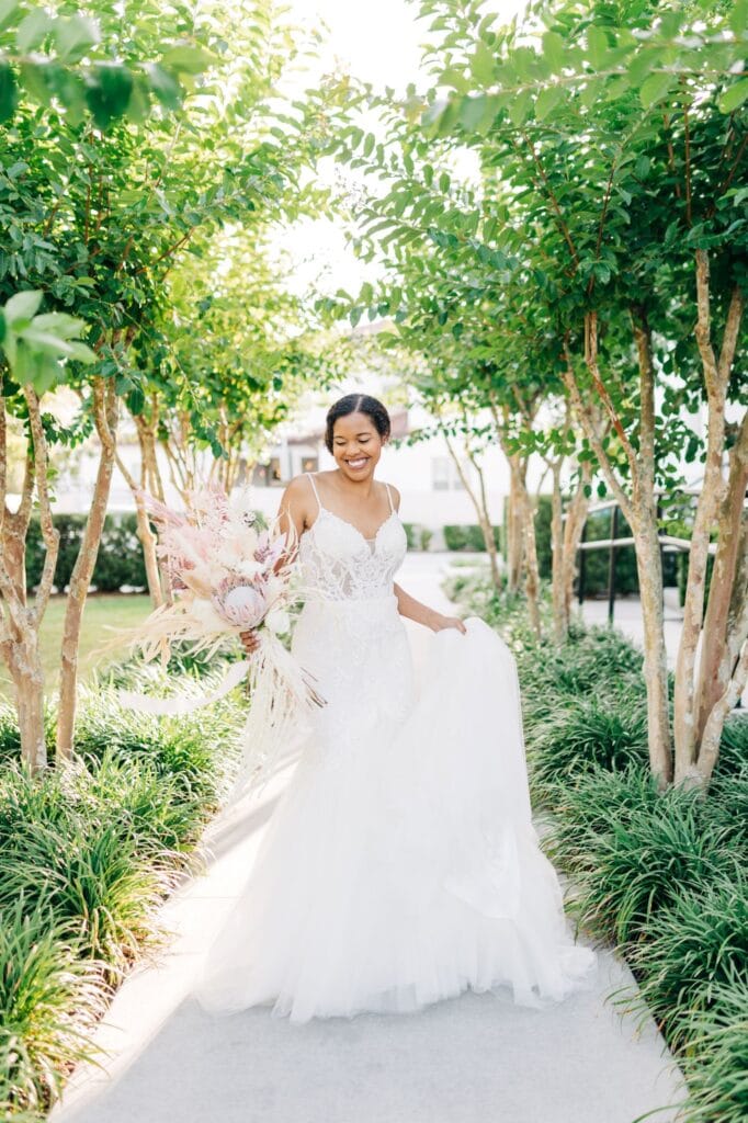 bride in a dress from Solutions Bridal standing and smiling on a sidewalk between several trees