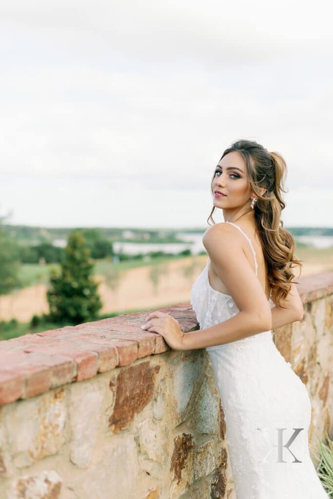 bride in a dress from Solutions Bridal leaning against a short stone wall